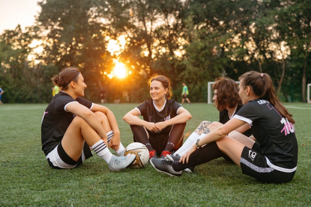 Four women soccer players resting and talking on the pitch