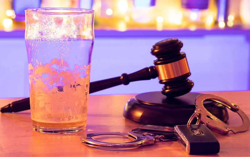 An empty beer glass, handcuffs, and a judge's gavel on a table.